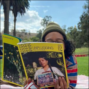 Cover of SALIMA Issue 2 being held up by Neko Natalia while reading in the park